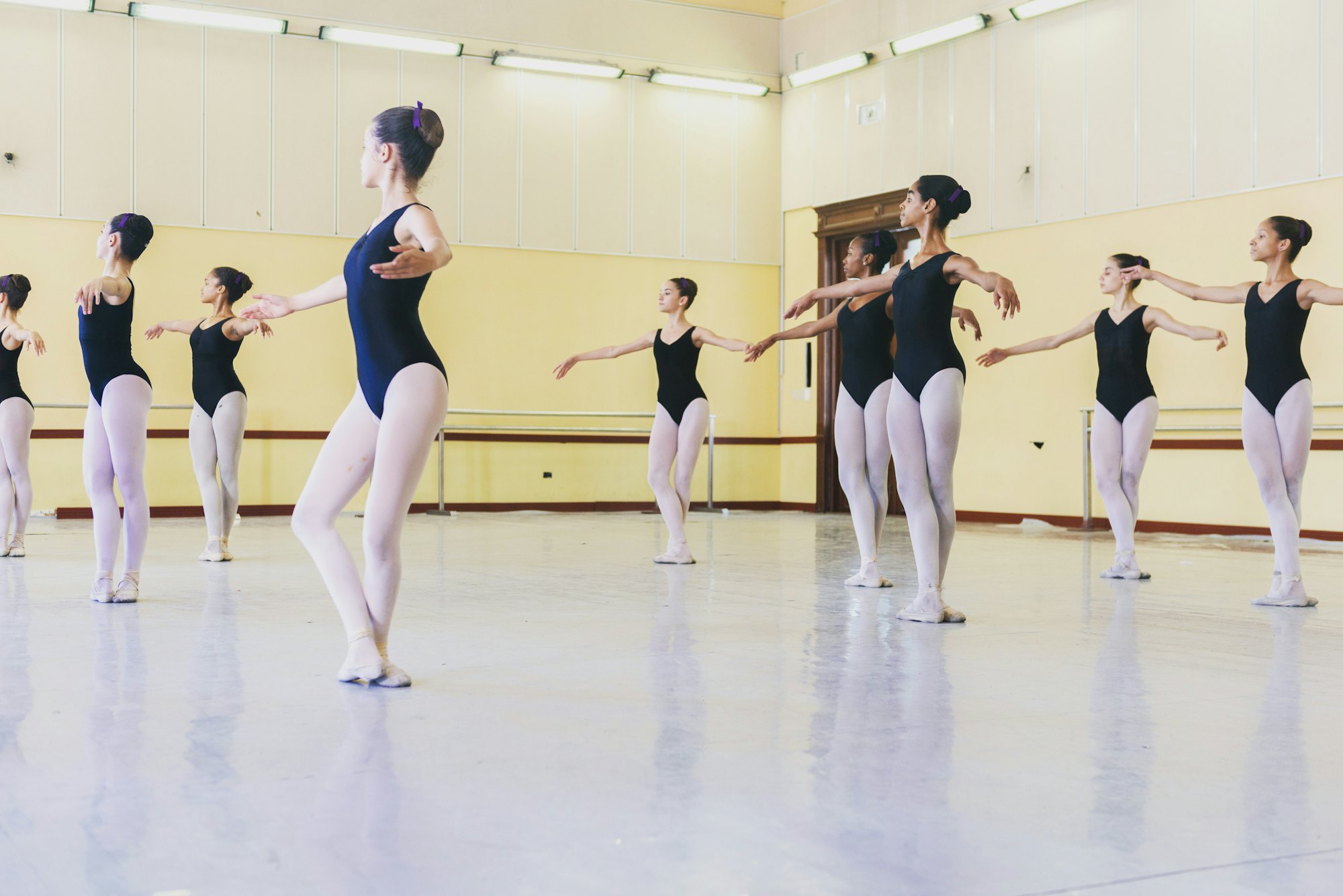 A ballet class practicing in a bright studio with barres along the walls